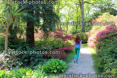 Stock image of girl walking along gravel pathway in garden, past flower borders