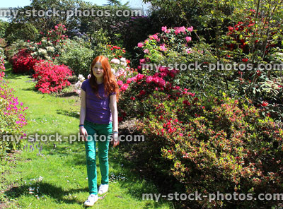 Stock image of girl walking along lawn pathway in garden with azaleas / rhododendrons