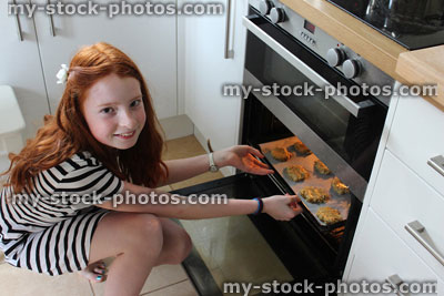 Stock image of girl baking in kitchen, putting biscuits in oven
