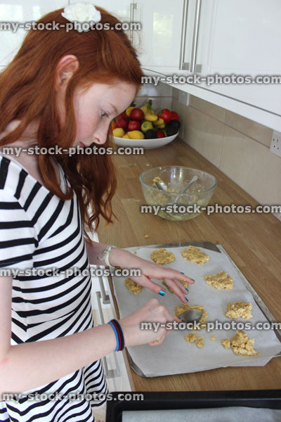 Stock image of girl baking in kitchen, spoon biscuit mixture onto oven tray