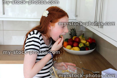 Stock image of young girl baking in kitchen, tasting cookie dough