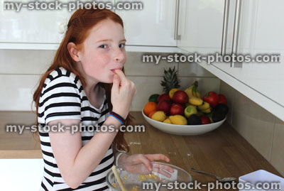 Stock image of young girl baking in kitchen, tasting biscuit mixture