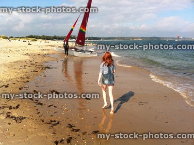 Stock image of red haired girl approaching red sailed yacht on beach