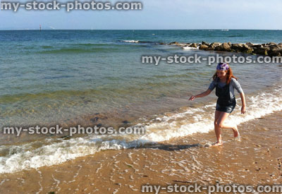 Stock image of red haired girl running through waves on beach
