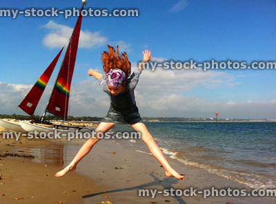 Stock image of red head girl jumping on a beach near a boat