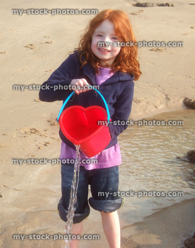 Stock image of young girl playing on Cornish beach, pouring water from bucket