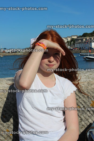 Stock image of girl at seaside, looking forward, shading eyes from sun with hand