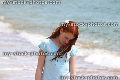 Stock image of girl standing on beach by sea, seaside summer holiday, looking down