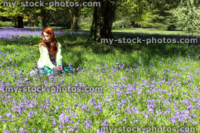 Stock image of girl with long hair sitting amongst woodland bluebells, dappled shade