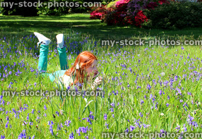 Stock image of girl with long hair lying amongst woodland bluebells, dappled shade
