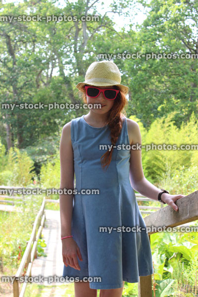Stock image of girl standing in garden on sunny day, hat, sunglasses, summer dress