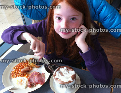 Stock image of girl eating full English fried breakfast, hot chocolate