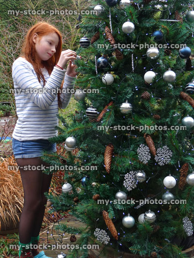 Stock image of girl hanging bauble decorations on outside Christmas tree