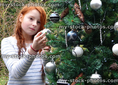 Stock image of girl hanging bauble decorations on garden Christmas tree