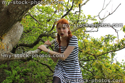 Stock image of tomboy girl climbing oak tree wearing stripy dress, worried, panicking