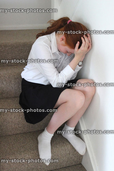 Stock image of upset girl crying on stairs, head in hands