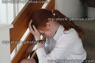 Stock image of upset girl crying on stairs, head in hands