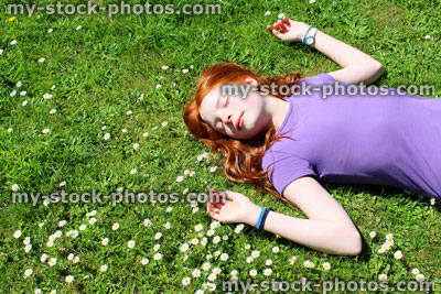 Stock image of young girl lying asleep / sunbathing in grass field of daisies