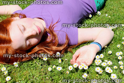 Stock image of girl with shiny red hair sunbathing in field, daisy flowers