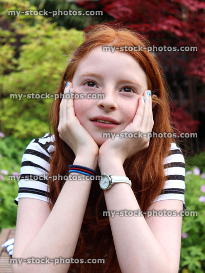 Stock image of happy girl daydreaming in garden, with head resting in hands