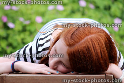 Stock image of girl lying on wooden bench, looking sideways, daydreaming