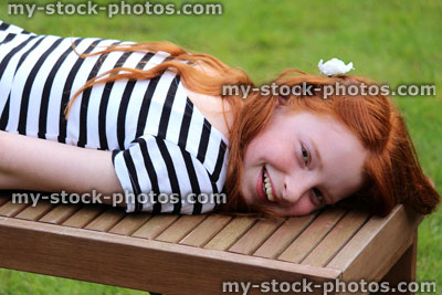 Stock image of girl lying on wooden bench on garden lawn