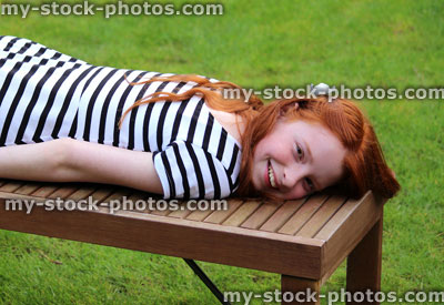 Stock image of girl lying on wooden bench on garden lawn