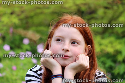 Stock image of happy girl daydreaming in garden, with head resting in hands