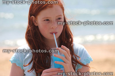 Stock image of girl drinking slushie drink with straw on beach, frozen ice drink