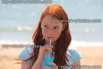 Stock image of girl drinking slushie drink with straw on beach, frozen ice drink