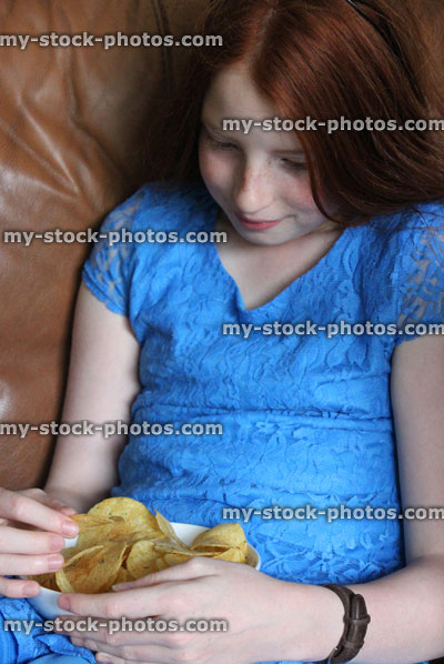 Stock image of girl eating crips on sofa, snacking, watching television