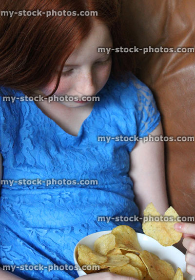 Stock image of girl eating crips on sofa, snacking, watching television