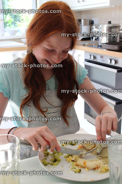 Stock image of girl eating fish pie dinner at kitchen table
