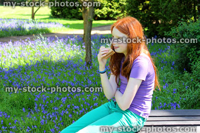 Stock image of girl eating sandwich on picnic table, in garden with bluebells