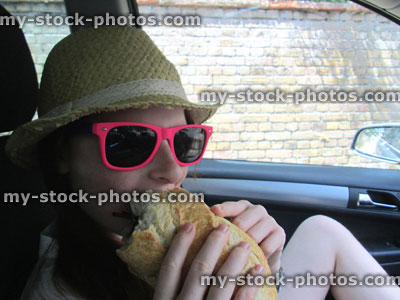 Stock image of girl eating large cheese salad sandwich in car
