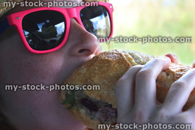 Stock image of girl wearing pink sunglasses, eating ham sandwich / baguette