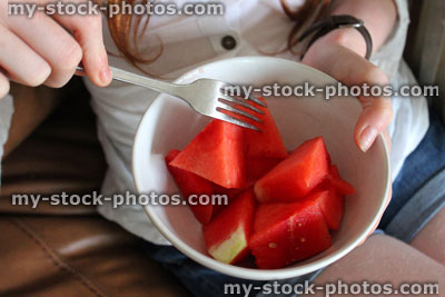 Stock image of girl on sofa eating healthy snack, chopped watermelon pieces