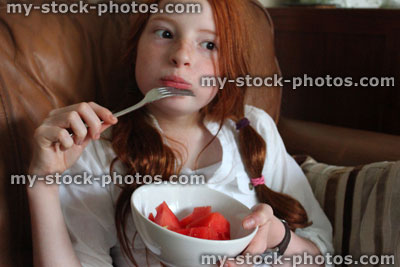 Stock image of girl on sofa eating healthy snack, chopped watermelon pieces