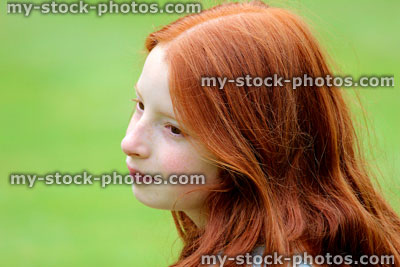 Stock image of young girl with long red hair smiling in garden, daydreaming