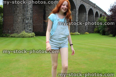 Stock image of girl playing in gardens, wearing short denim dungarees