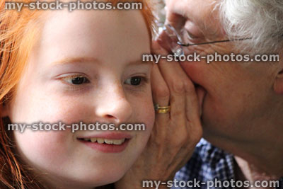 Stock image of grandmother whispering secret in young granddaughter's ear, listening
