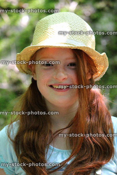 Stock image of pretty girl smiling in sunshine, long red hair, pigtails, straw hat