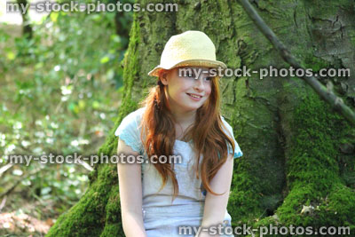 Stock image of girl in woodland forest, straw hat, sitting, looking, daydreaming, tree trunk