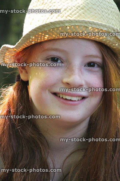 Stock image of pretty young girl smiling in sunshine, long red hair, straw hat