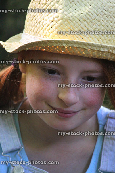 Stock image of pretty young girl smiling in sunshine, long red hair, straw hat, looking down
