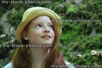 Stock image of girl in woodland forest, straw hat, sitting, looking up and daydreaming