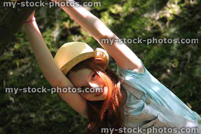 Stock image of girl in woodland forest, straw hat, standing, swinging, hanging from branch
