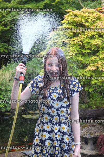 Stock image of girl soaking herself with garden hose as fountain