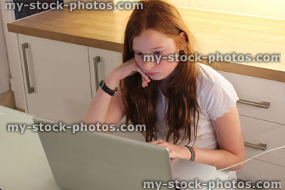 Stock image of girl using laptop computer in kitchen for school homework, studying