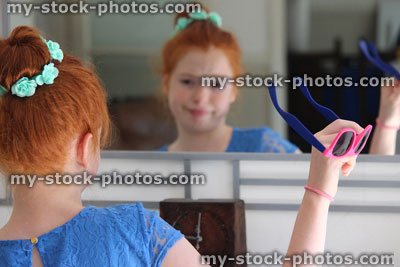 Stock image of girl with red hair in bun, looking in mirror, sunglasses
